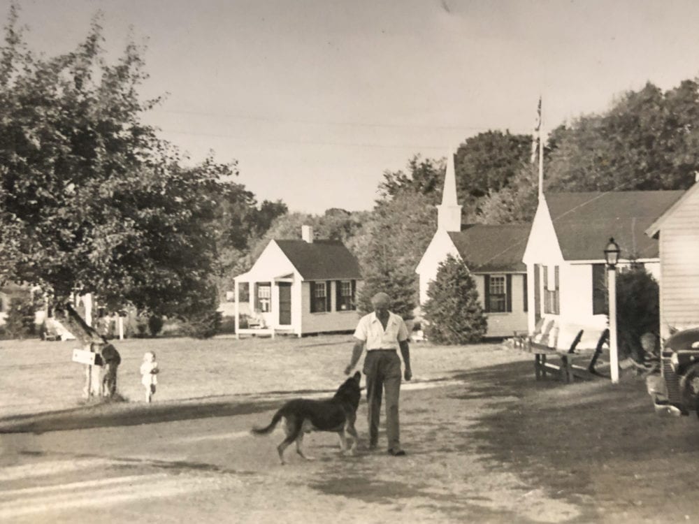 Herbert Plimpton playing with a dog in front of New England Village